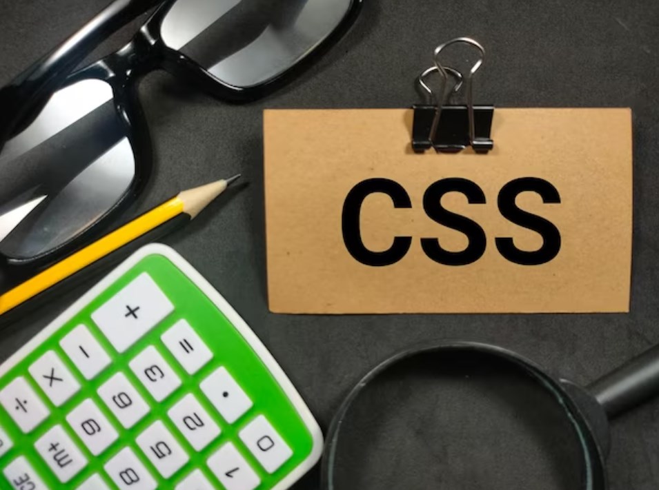 a calculator, glasses, a pencil, a magnifying glass, and a card that says “CSS” on a black table