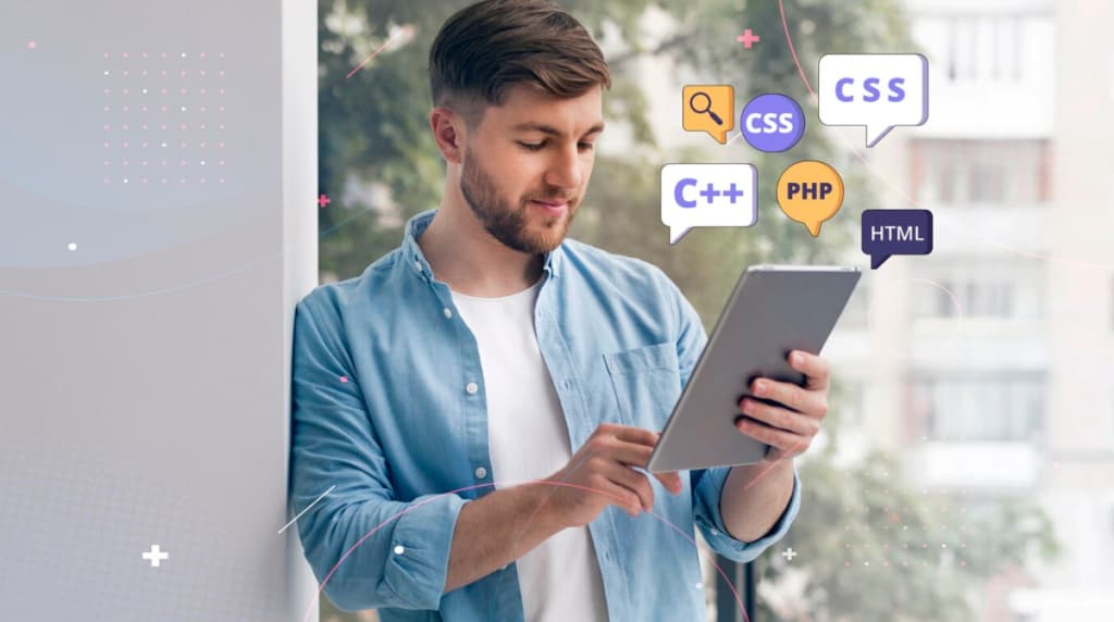 A man in a blue shirt focused on his tablet with floating programming language logos