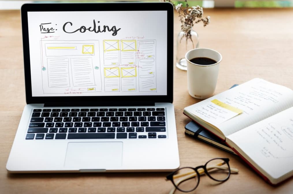 A laptop screen shows a webpage wireframe next to notes
