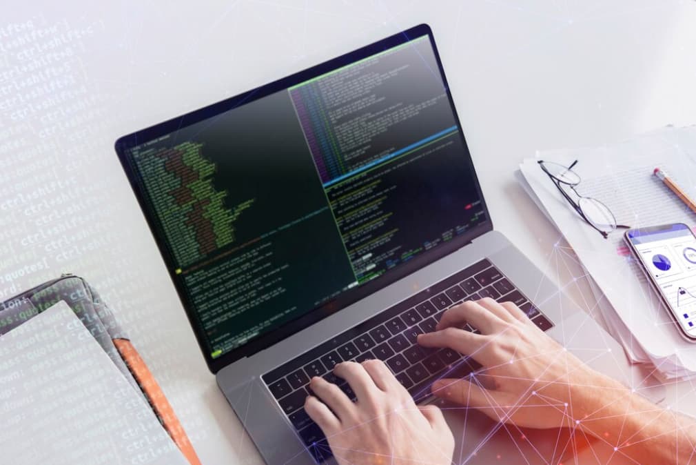 Hands typing on a laptop with a coding interface and digital graphics