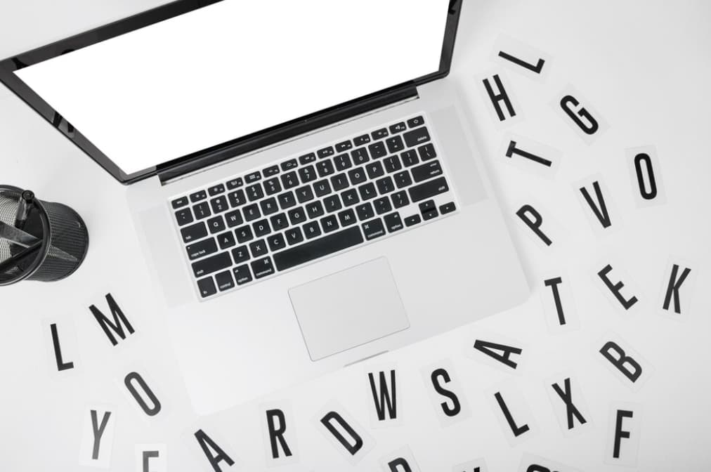 An open laptop with scattered letter cutouts around it
